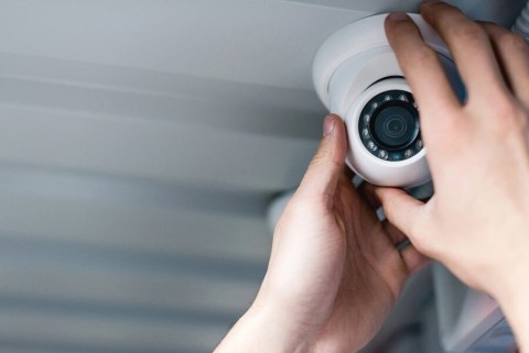 Hands shown installing a smart home security camera on an exterior ceiling.