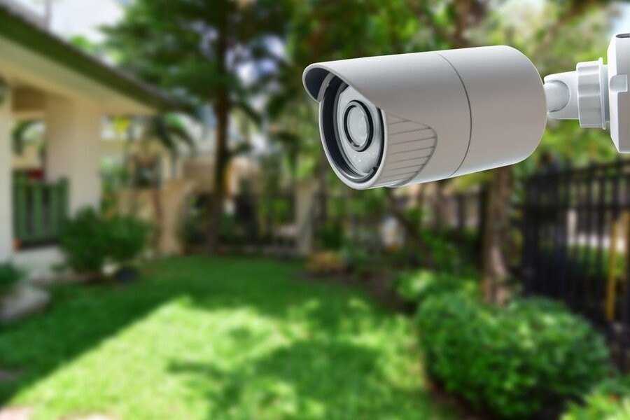 A smart home security camera over a backyard with vibrantly green grass.
