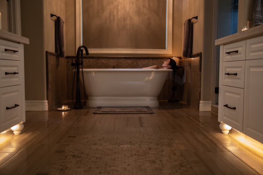 A woman relaxes in a bathtub. The bathroom is illuminated by soft, dimmed lights.