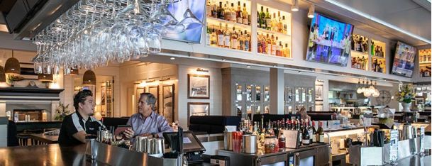 A vibrant bar area with hanging glasses, bright lighting, and a variety of displayed bottles.