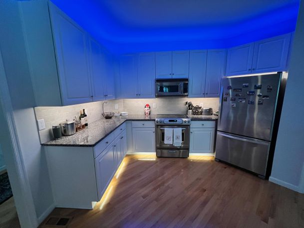 A modern kitchen illuminated with blue ambient lighting above the cabinets.