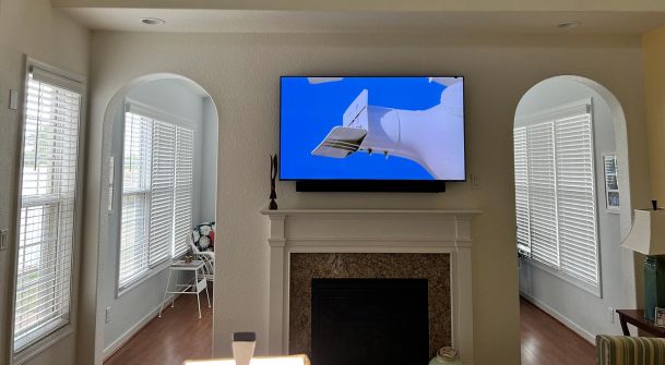 A TV mounted above a fireplace surrounded by natural light streaming through arched windows.