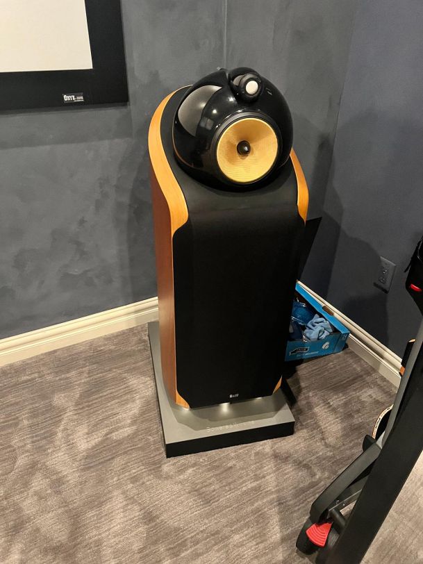 A high-end floor-standing speaker with a wooden cabinet and a dome tweeter in a home theater.