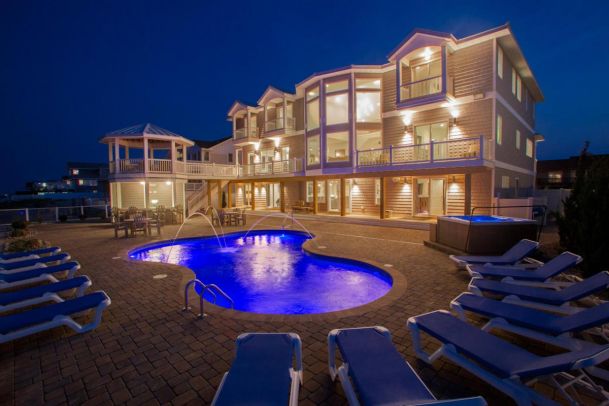 A large house with a glowing pool and outdoor fountains at night.