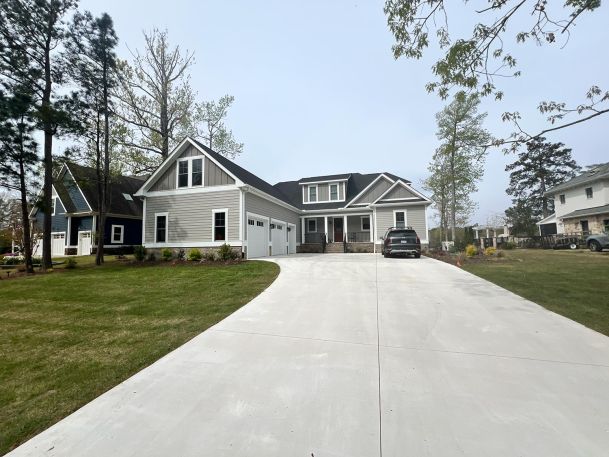 A wide driveway leading to a modern suburban house surrounded by trees and green lawns.