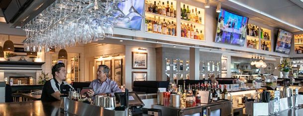 A vibrant bar area with hanging glasses, bright lighting, and a variety of displayed bottles.