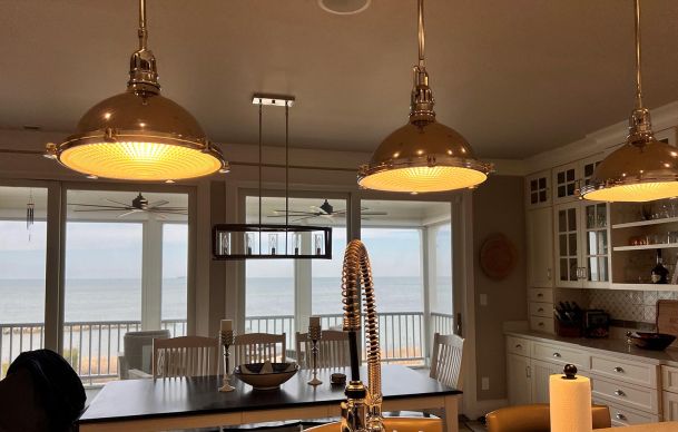 A kitchen with warm pendant lighting and a scenic ocean view through large windows.