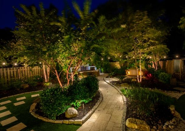 A serene backyard with a well-lit stone walkway and lush trees under a night sky.