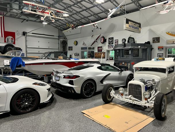 A spacious garage filled with classic cars, a speedboat, and vintage decor on the walls.