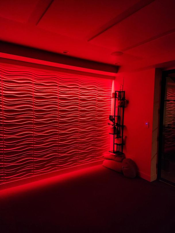 A room with a wavy textured wall illuminated by vivid red accent lighting.