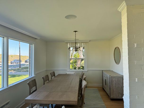 Dining room with a wooden table, chairs, chandelier, and a large window showcasing natural light.