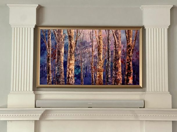 A framed painting of birch trees with vibrant colors mounted above a white fireplace.