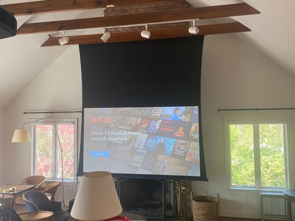 A retractable projector screen in a living room with exposed wooden beams.