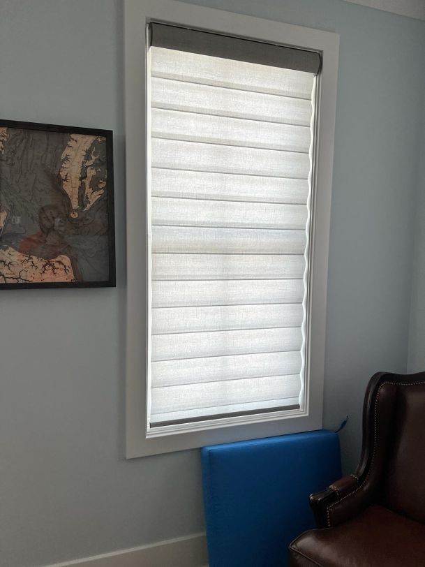 A Roman-style shade partially drawn over a window with light blue walls and a framed map nearby.