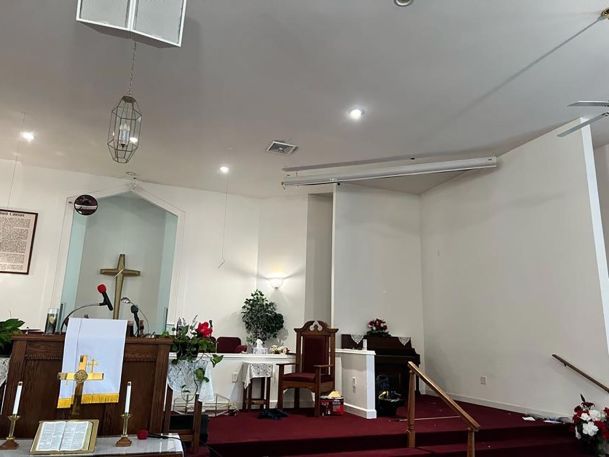 An empty church stage with red carpet, white walls, and a gold cross in the background.