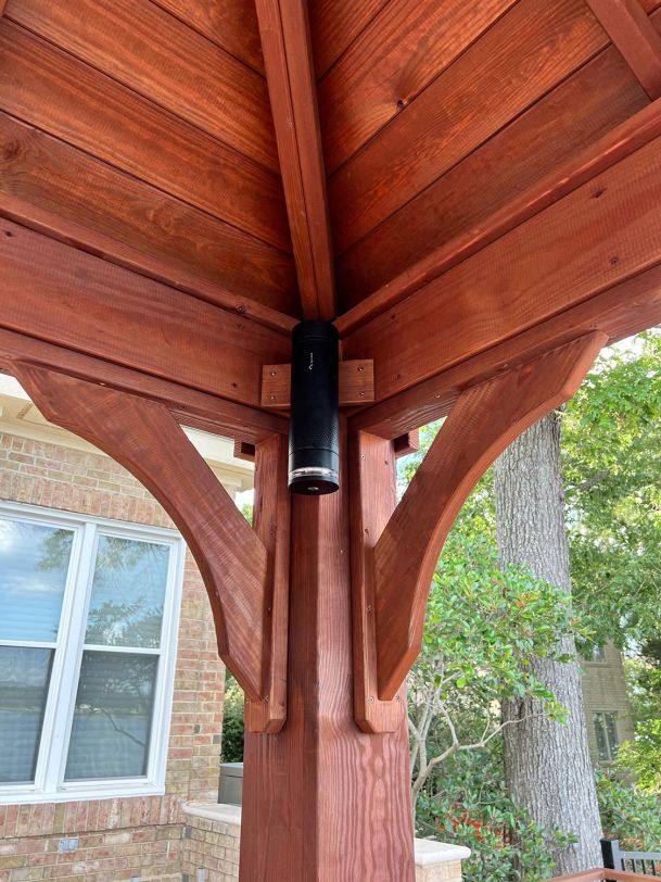 An outdoor wooden gazebo with a mounted cylindrical speaker at the top corner.