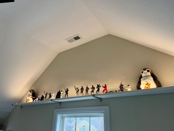 A high shelf featuring collectible figurines and plush toys in a vaulted-ceiling room.