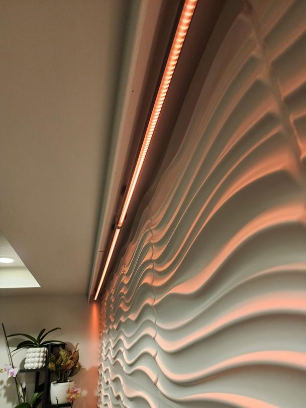 Close-up view of an LED strip light installed above a textured wave wall, creating a warm glow.