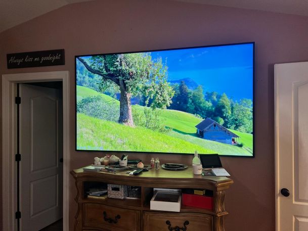 Large flat-screen TV mounted on the wall displaying a serene landscape of a tree and field.