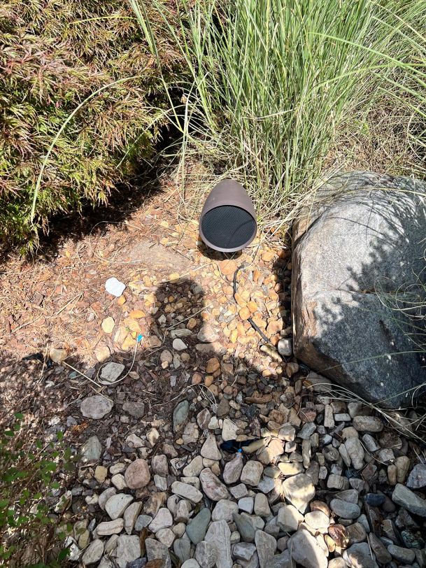 A discreet outdoor speaker placed among rocks and plants in a landscaped garden.