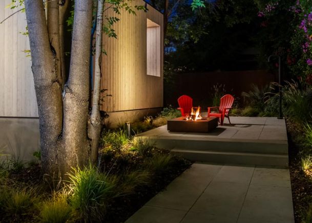 A serene backyard patio with a fire pit and two red chairs under the trees.