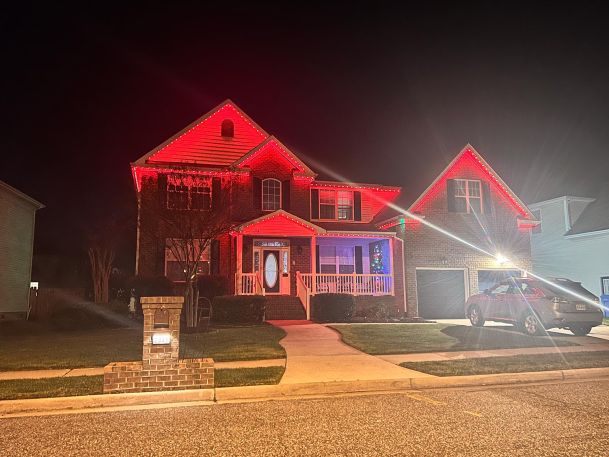 A house lit with red holiday-themed exterior lights, creating a festive atmosphere at night.