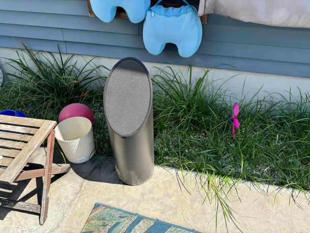 A cylindrical outdoor speaker placed on a concrete surface near grass.