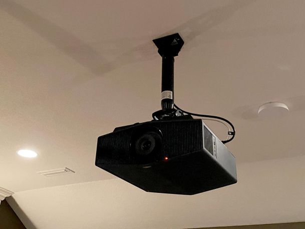 A ceiling-mounted black projector in a home theater room.