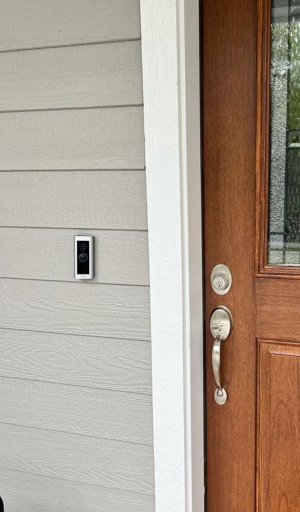 A modern front door with a sleek doorbell camera mounted on the siding next to it.