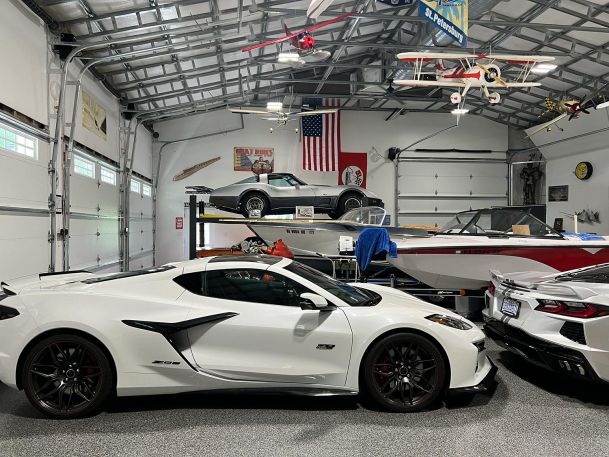 A garage interior with a car lift holding vintage vehicles and hanging model airplanes.