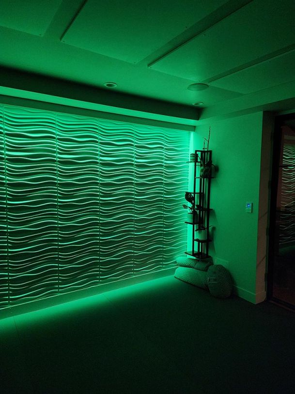 A wavy textured wall bathed in green accent lighting with a modern decor piece on the side.