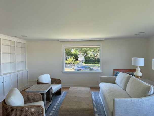 Minimalistic living room with a large window, sofa, chairs, and built-in white shelving.